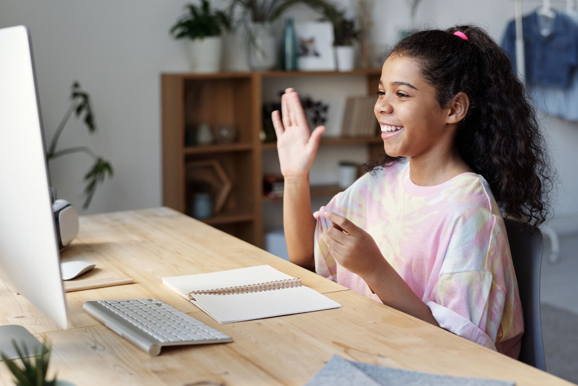 A smiling girl raising her hand to answer in her online class