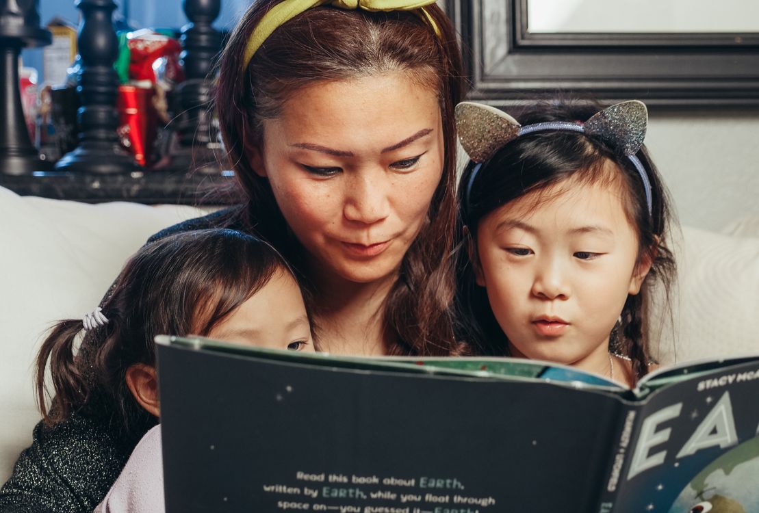 A mother and her two daughters reading a book together