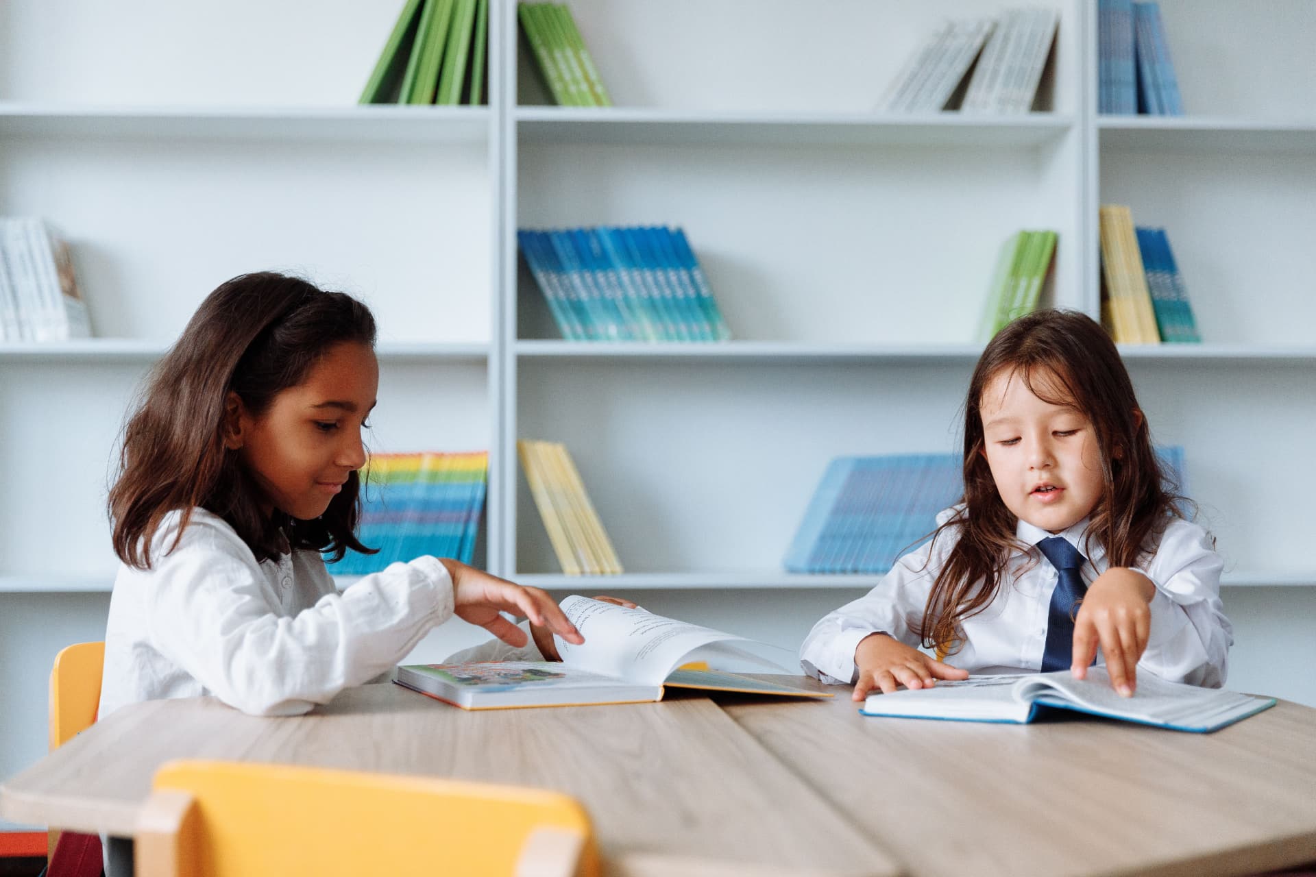 Two schoolgirls reading books together at a table