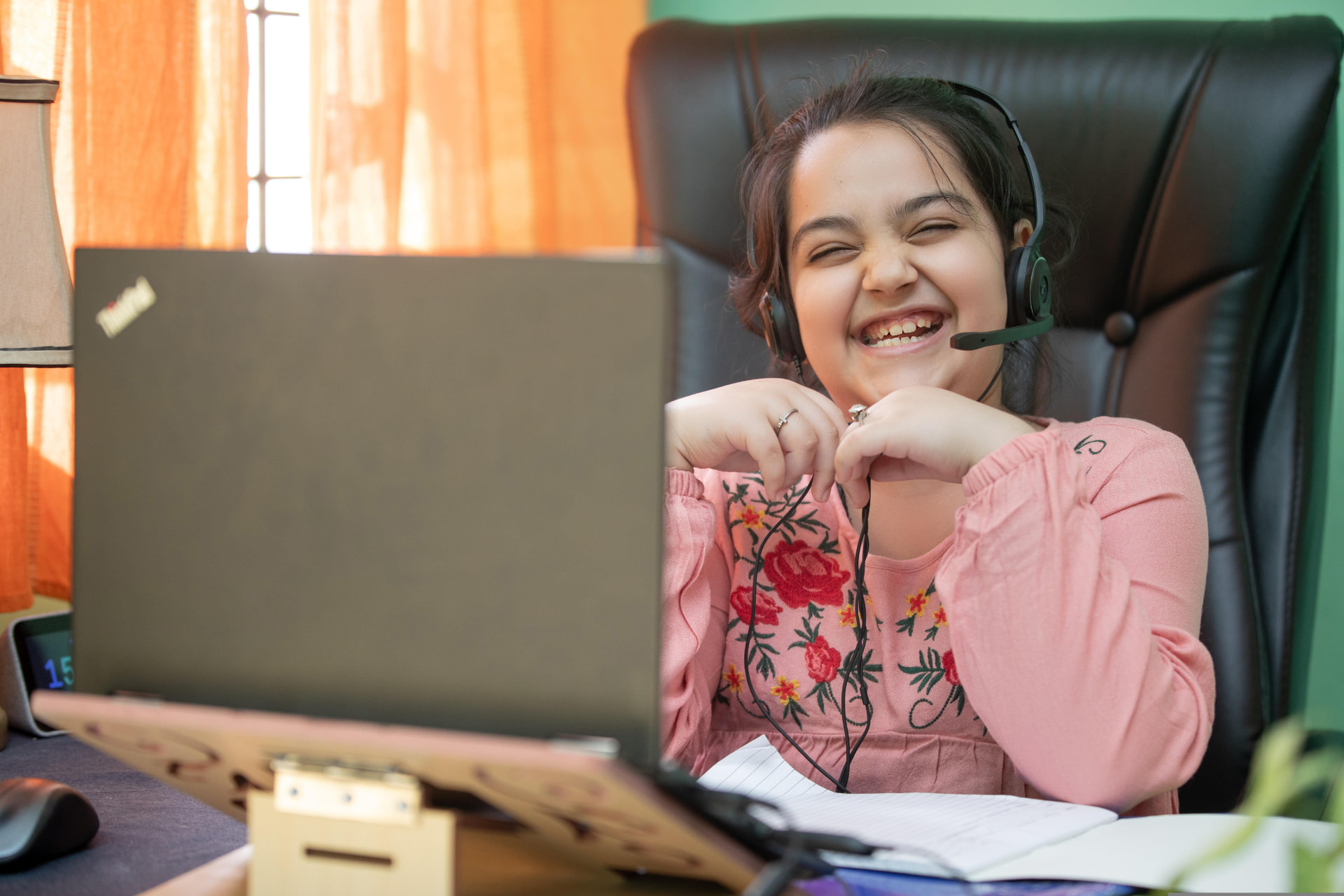 A girl laughing with delight during her online class, wearing a headset