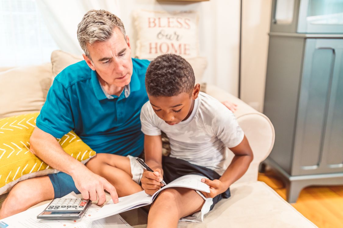 A father helping a boy write in his workbook